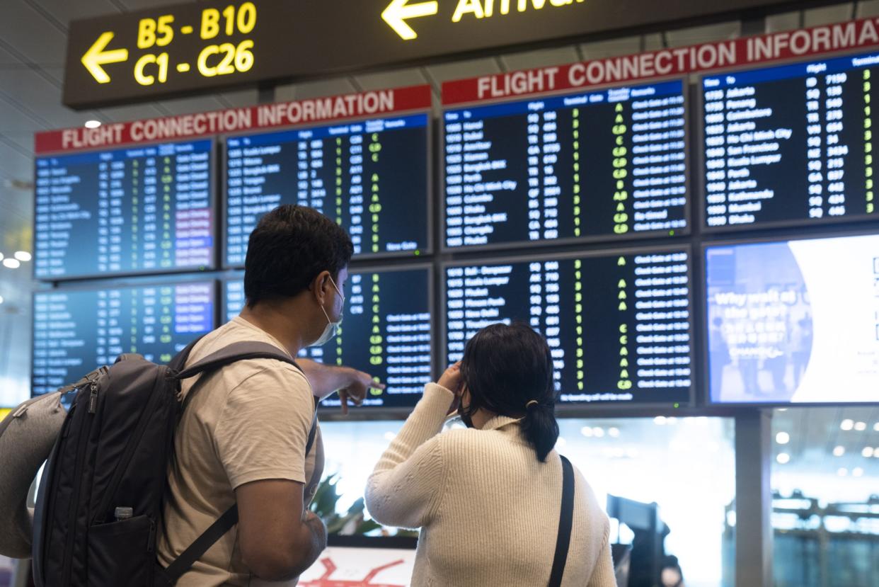 Travellers in front of a flight information panel at Changi Airport in Singapore, on Wednesday, March 30, 2022.  (Photo: Ore Huiying/Bloomberg)