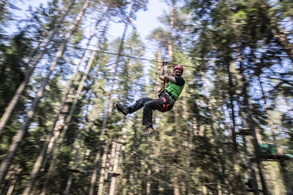 In this image take on Thursday, April 23, 2020 Diego Fregona, 58, adventure park owner slips on a pulley of the park, in Clusone, near Bergamo, northern Italy. Fregona spent all his savings to repair the damage done to his 10.000sqm park after a whirlwind in October knocked down trees, climbing ropes and suspended trails, only to remain closed with very little money and lots of doubts as to whether he'll ever be able to restart. His words for the Associated Press were "There isn't a family who didn't have a bereavement, the only thing left to do is to get up again." (AP Photo/Luca Bruno)