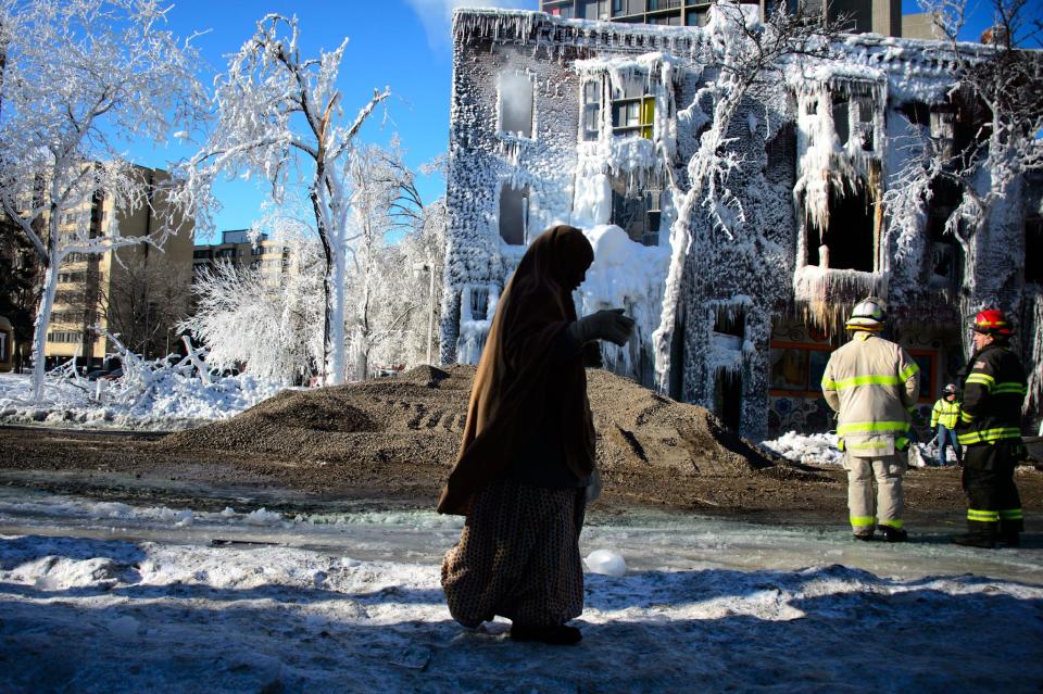 A pedestrian makes her along the icy sidewalk as firefighters look over the scene on Thursday, Jan. 2, 2014, in Minneapolis, after Wednesday's fire destroyed the apartment building. Fourteen were injured and the cause of the fire is still unclear. (AP Photo/The Star Tribune, Glen Stubbe) MANDATORY CREDIT; ST. PAUL PIONEER PRESS OUT; MAGS OUT; TWIN CITIES TV OUT