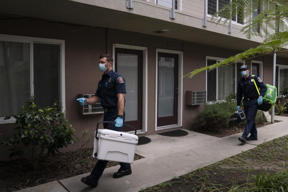 Torrance firefighter Trevor Borello, left, carries a cooler containing the Pfizer COVID-19 vaccine as he walks to an apartment to inoculate two sisters who have muscular dystrophy, Wednesday, May 12, 2021, in Torrance, Calif. Teamed up with the Torrance Fire Department, Torrance Memorial Medical Center started inoculating people at home in March, identifying people through a city hotline, county health department, senior centers and doctor's offices, said Mei Tsai, the pharmacist who coordinates the program. (AP Photo/Jae C. Hong)