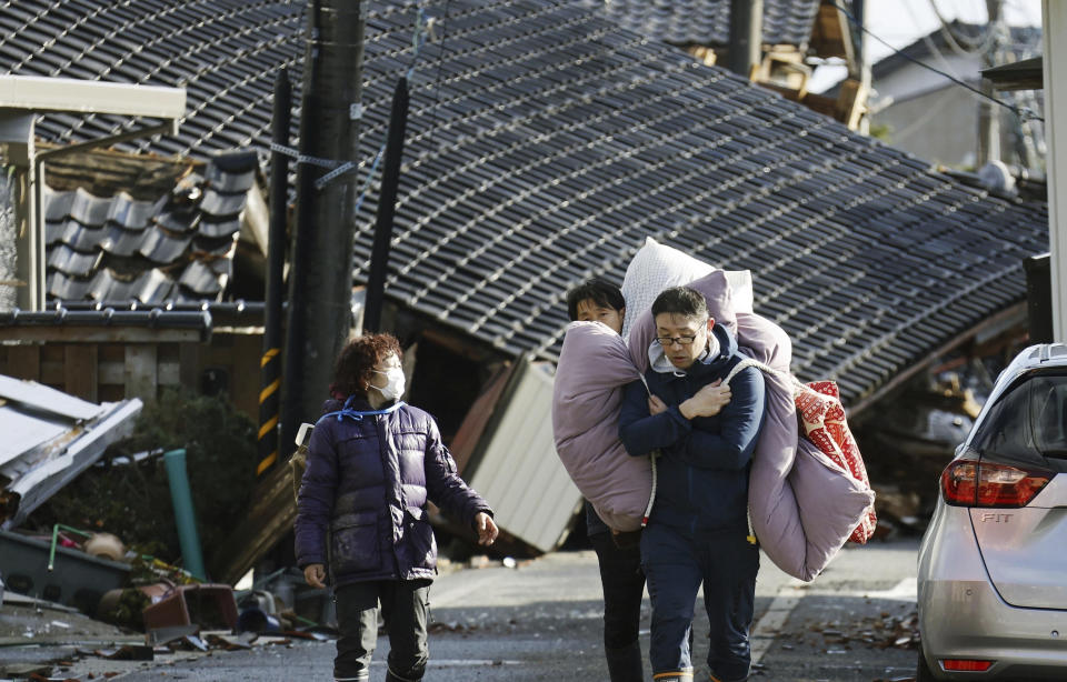 Dos personas cargan con ropa de cama entre las casas derribadas por sismos y tsunami en Suzu, en la prefectura de Ishikawa, Japón, el 4 de enero de 2024. (Kyodo News vía AP)