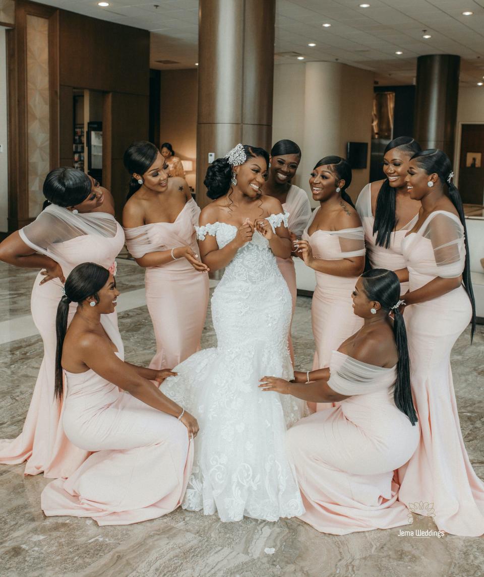 A bride smiles as her bridesmaids look at her and fix her dress.