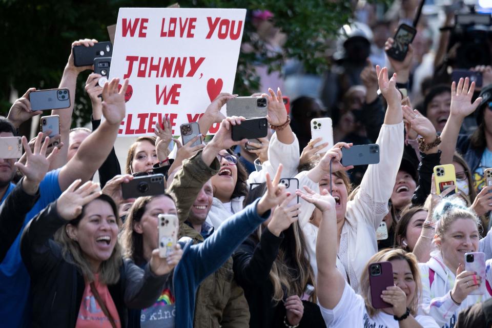 A throng of fans have their phones out to take pictures, with one holding up a sign that says "We love you Johnny, we believe you"