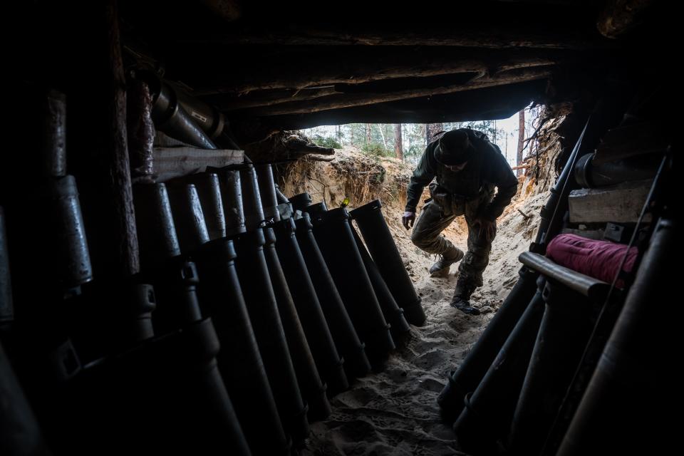 A serviceman ducking down to enter a trench that's filled with ammunition.