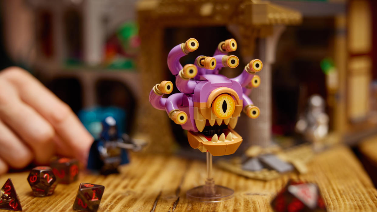  Lego Beholder on a table covered with dice, with a nearby hand holding a minifigure. 