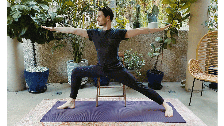 Man seated on a chair while practicing Warrior 2 Pose in yoga