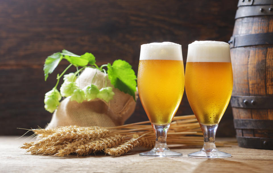 Vasos fríos de cerveza, espigas de trigo, lúpulo y barril de cerveza sobre un fondo de madera.