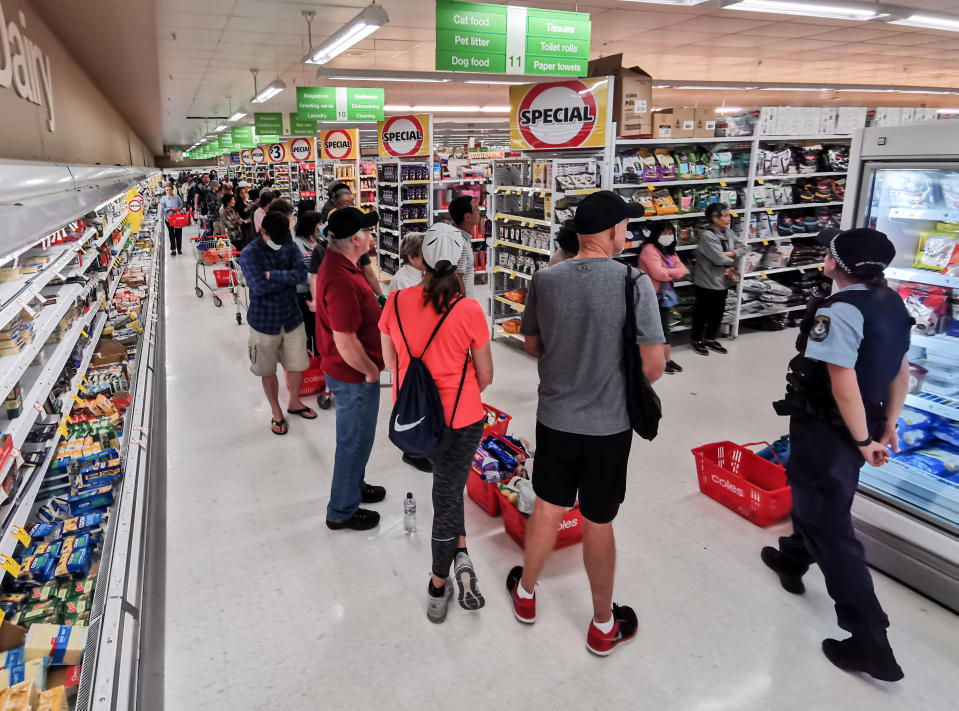 A Police Officer watches on at people queueing for a delivery of toilet paper, paper towel and pasta at Coles Supermarket, Epping in Sydney, Friday, March 20, 2020. Supermarkets have been struggling to keep up with demand for products such as toilet paper in recent days, as panic buying as a result of the Covid-19 pandemic has resulted in people purchasing far more than usual. Supermarkets have put in place limits on the quantity people can purchase of many everyday items. (AAP Image/James Gourley) NO ARCHIVING