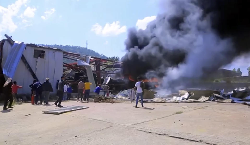 In this image made from video, people look on as a car factory burns in Mekele, Ethiopia, Wednesday, Oct. 20, 2021. Residents say new airstrikes have hit the capital of Ethiopia’s Tigray region as exclusive video shows injured people with bloodied faces being carried into ambulances. Ethiopia's government says it targeted facilities for making and repairing weapons, while a Tigray spokesman denies it. (AP Photo)