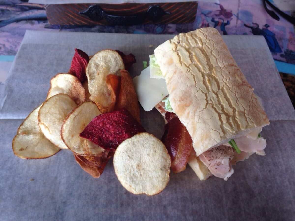 The Dutch Crunch Sandwich with colorful potato chips on a white serving paper, Trencher's Deli, Tulsa, Oklahoma, on a purple and blue intricate tablecloth