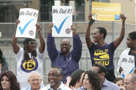 People hold up signs at a celebration event for the signing of an ordinance raising the city's minimum wage to $15 an hour by 2020 from the current $9 in Los Angeles, California June 13, 2015. REUTERS/Jonathan Alcorn