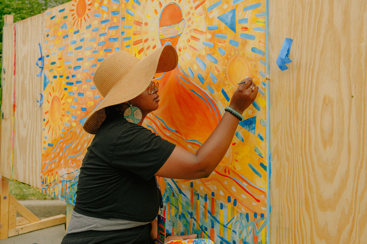 A person wearing a large sunhat paints a mural on a wooden board (Mahdi Atif for NBC News)