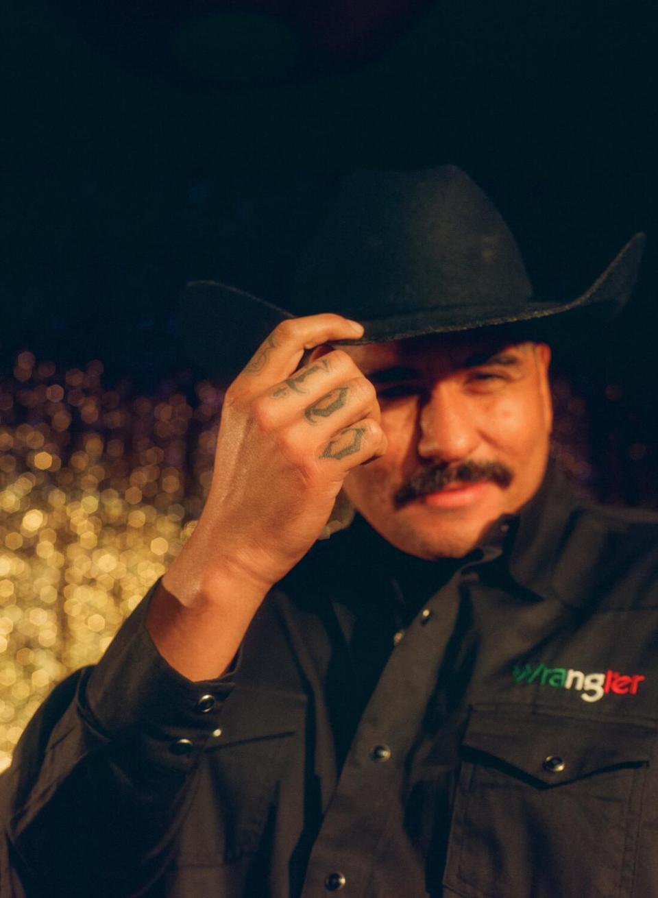 A man winks at the camera, wearing a black cowboy hat