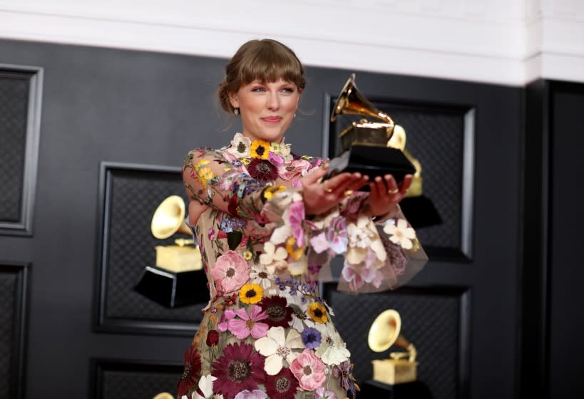 Taylor Swift holding her Grammy trophy on a red carpet