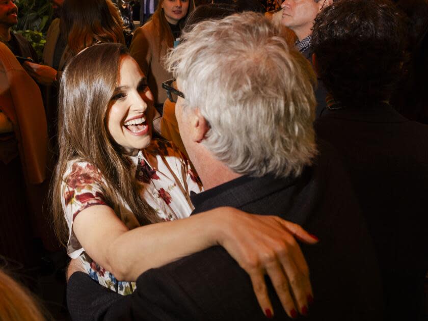 A smiling woman greets a gray-haired man who's seen from behind