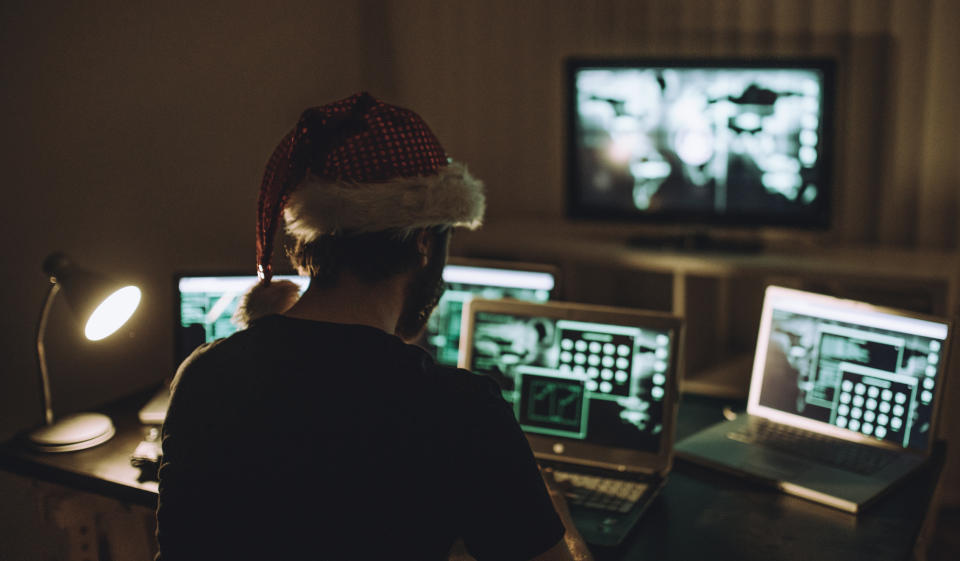 A person wearing a Santa hat sitting in front of computers in a dark room.