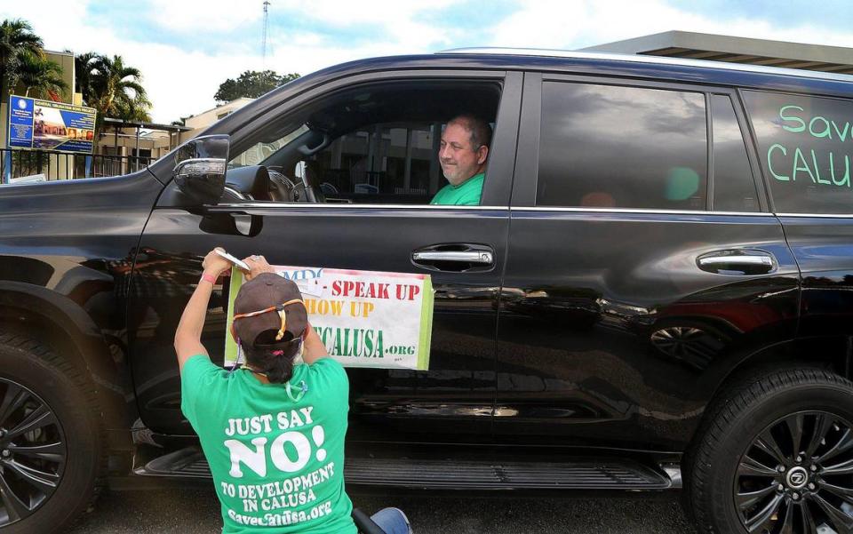 Sandy Lea-Oquendo tapes a poster on James Ritter’s car as residents of the Calusa neighborhood in Kendall prepared for a drive-through rally, part of their Save Calusa campaign in opposition to a housing development on the defunct golf course.