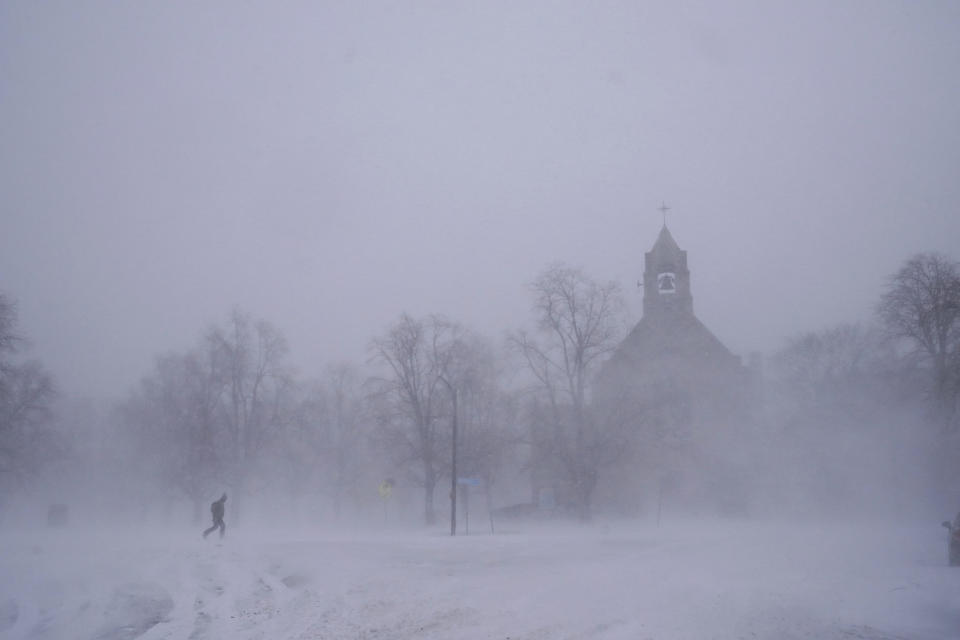 FILE - A lone pedestrian in snow shoes makes his way across Colonial Circle as St. John's Grace Episcopal Church rises above the blowing snow amid blizzard conditions in Buffalo, N.Y. on Saturday, Dec. 24, 2022. The Buffalo Bills have been a reliable bright spot for a city that has been shaken by a racist mass shooting and back-to-back snowstorms in recent months. So when Bills safety Damar Hamlin was critically hurt in a game Monday, the city quickly looked for ways to support the team. (Derek Gee/The Buffalo News via AP, File)