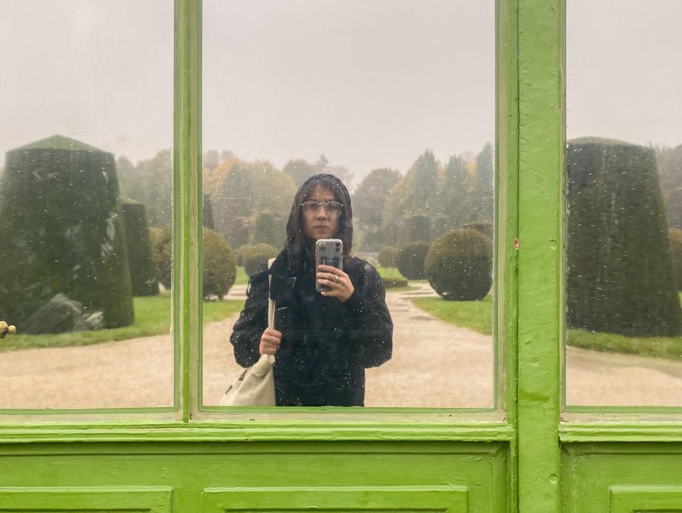 The author takes a selfie in front of a window reflecting trees behind her on a lime green door