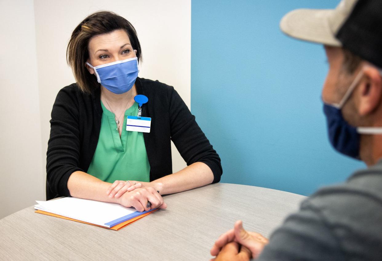 woman in Her Forties Wearing a Face Mask Talks with a Masked White Male in His Forties while Sitting at a Table in an office