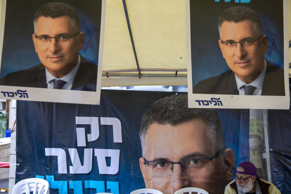 A Likud party member sits by a poster of veteran politician Gideon Saar from the governing Likud Party at a voting center in the northern Israeli city of Hadera, Thursday, Dec. 26, 2019. Israel's governing Likud party was holding primaries on Thursday, in the first serious internal challenge to Israeli Prime Minister Benjamin Netanyahu in his more than a decade in power. Saar hopes to unseat Netanyahu, arguing that he will be better placed to form a government in national elections in March after Netanyahu failed to do so in two repeat elections this year. (AP Photo/Ariel Schalit)