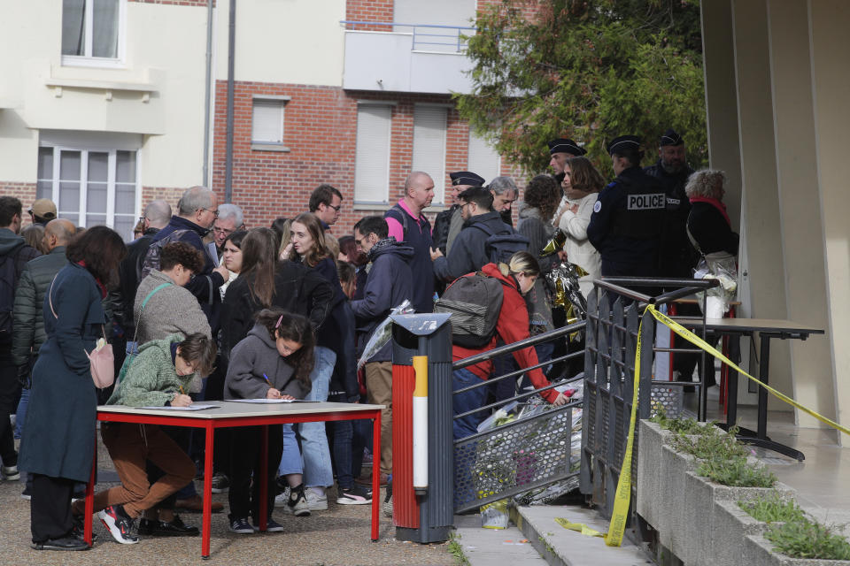 Children sign documents as people place flowers at the Gambetta high school after a bomb alert Monday, Oct. 16, 2023 in Arras, northern France. French authorities say the high school where a teacher was fatally stabbed in an attack last week has been evacuated over a bomb alert, as France's President cut short travel plans abroad to host a security meeting Monday.(AP Photo/Michel Spingler)