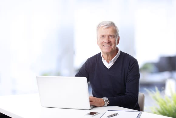 Older man sitting at a laptop, smiling