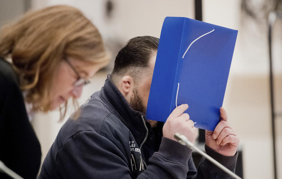 The defandant covers his face with a folder as he arrives at the temporay Oldenburg district court at the Weser Ems halls in Oldenburg, Germany, Tuesday, Oct. 30, 2018. The nurse serving a life sentence for two murders is going on trial on charges that he killed a further 100 patients at two hospitals in Germany. (Julian Stratenschulte/dpa via AP, Pool)