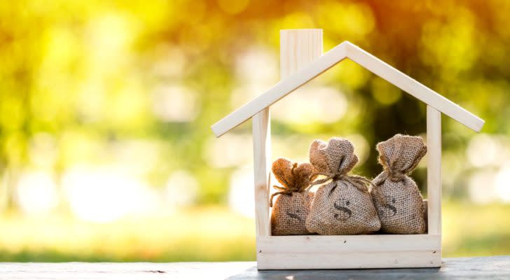 a wooden house shape holds 3 bags of cash representing reits to buy
