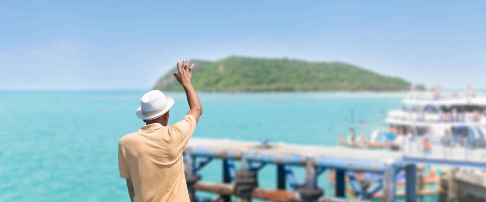 The traveler man standing on the boat waving his hand, greeting or goodbye to their friends on the pier.