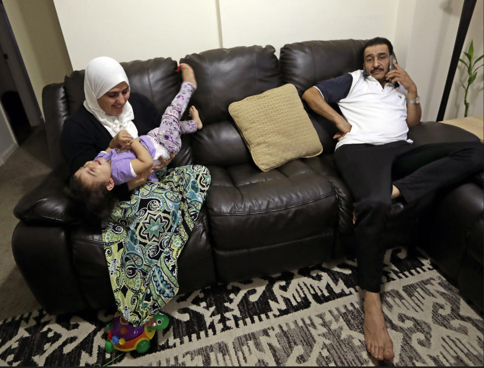 In this Sunday, Aug. 25, 2019, photo, Diaa Alhanoun, right, a Syrian refuge chef, slumps into the couch at home while talking to his brother, now living in Jordan after fleeing Syria during the country's civil war, as Alhanoun's wife, Fatima Kwara plays with their young daughter, Masa, at the family's Staten Island home in New York. Masa, which means "Diamond," was born in the United States. (AP Photo/Kathy Willens)