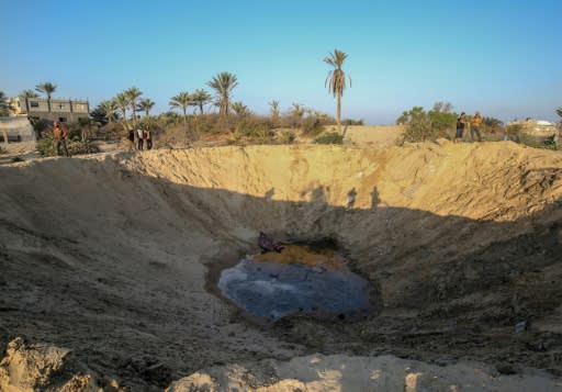 Palestinian onlookers inspect a large crater one of the Israeli strikes scoured out of the sandy Gaza soil