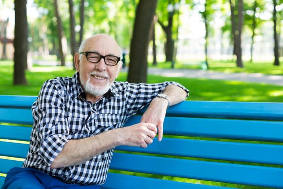 Smiling older man sitting on blue bench outdoors