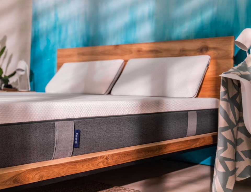 Picture of wooden bedframe and an emma mattress, against a blue toned wall