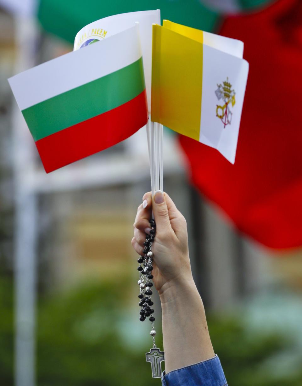 A woman holds up a rosary, along with the Vatican and Bulgaria flags, in Sofia, Bulgaria, Sunday, May 5, 2019. Pope Francis is visiting Bulgaria, the European Union's poorest country and one that has taken a hard line against migrants, a stance that conflicts with the pontiff's view that reaching out to vulnerable people is a moral imperative. (AP Photo/Alessandra Tarantino)