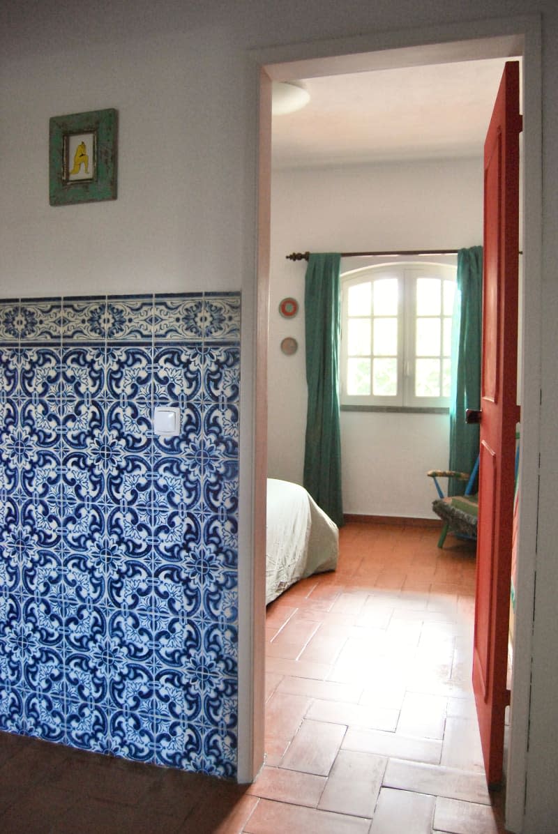 View of bedroom with teal curtains from hallway with blue tiled wall.