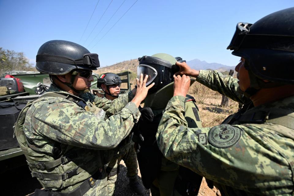 Soldiers help another soldier put on equipment