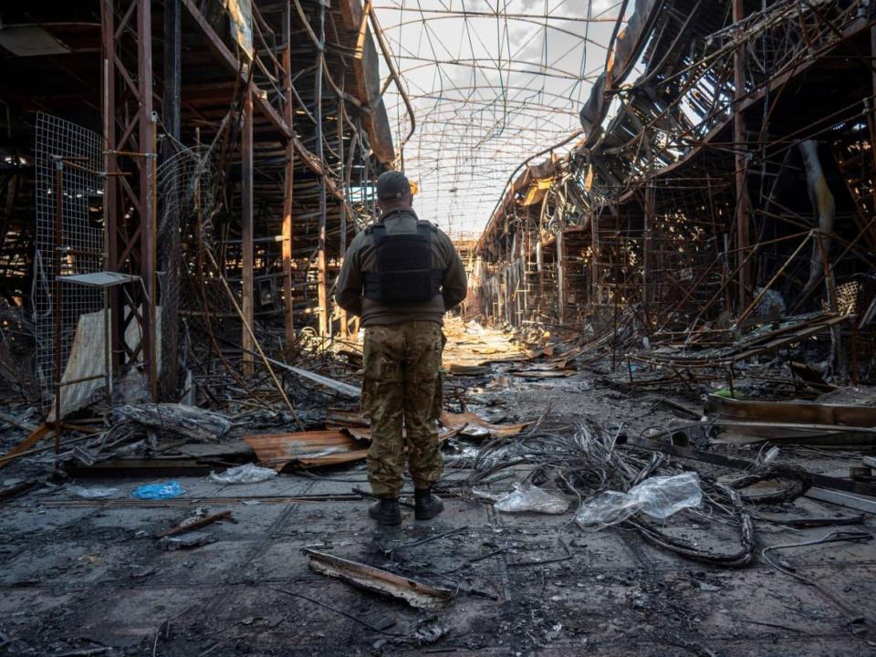 A Ukrainian police officer documents shell damage at a clothing market in Kharkiv. Volunteers in the city have been running a food service for soldiers, emergency workers and civilians in need. (Sergey Bobok/AFP/Getty Images - image credit)