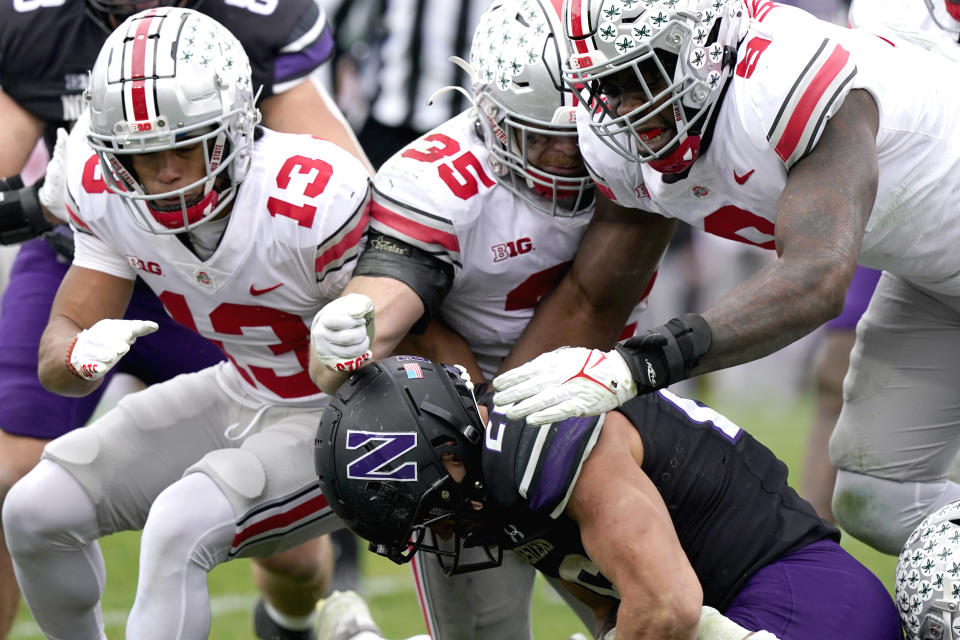 Northwestern running back Evan Hull, bottom, is tackled by Ohio State safety Cameron Martinez, left, linebacker Tommy Eichenberg and defensive end Zach Harrison, right, during the second half of an NCAA college football game, Saturday, Nov. 5, 2022, in Evanston, Ill. (AP Photo/Nam Y. Huh)