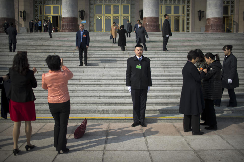 A security official stands guard as delegates pose for photos on the steps of the Great Hall of the People after a meeting one day ahead of the opening session of China's National People's Congress (NPC) in Beijing, Monday, March 4, 2019. A year since removing any legal barrier to remaining China's leader for life, Xi Jinping appears firmly in charge, despite a slowing economy, an ongoing trade war with the U.S. and rumbles of discontent over his concentration of power. (AP Photo/Mark Schiefelbein)