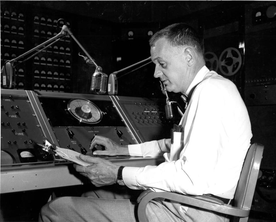 a man in a button down shirt and tie sits in a control room during operation plumbob