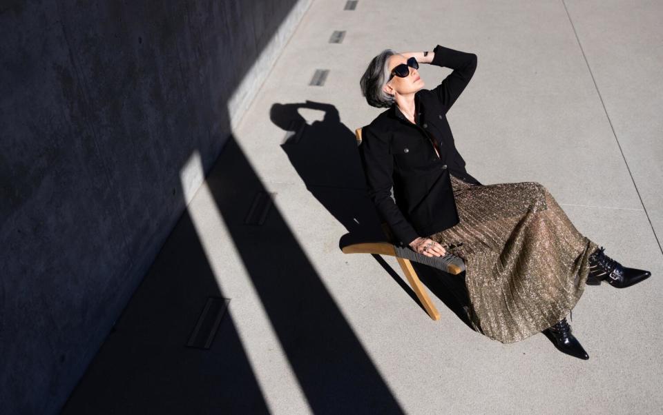 Seen from above, a woman in sunglasses sits on a chair and rests her hand near her forehead.