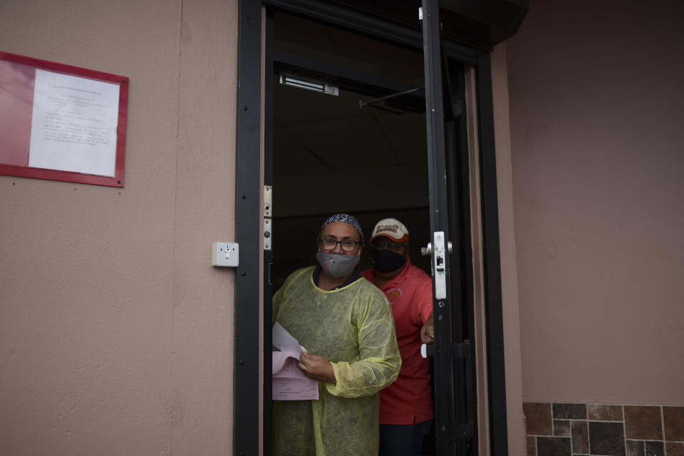 Sandra Algarin and Efrain Ortiz, employees at a health clinic, peek out the door while wearing masks as a precaution against COVID-19, in Canovanas, Puerto Rico, Thursday, May 21, 2020. Puerto Rico is cautiously reopening beaches, restaurants, churches, malls, and hair salons under strict conditions as the U.S. territory emerges from a two-month lockdown despite dozens of new coronavirus cases reported daily. (AP Photo/Carlos Giusti) PUERTO RICO OUT-NO PUBLICAR EN PUERTO RICO