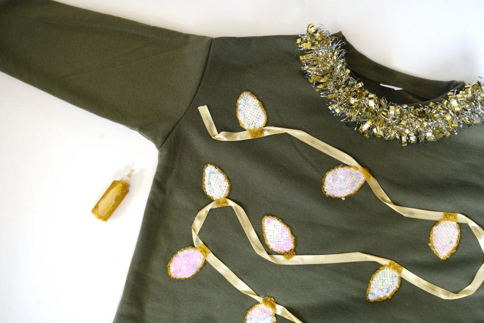 Using gold puff paint to create holiday lights design on DIY Christmas sweater.