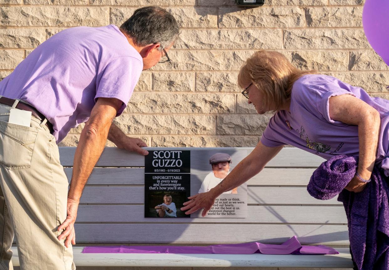 Bob and Paula Guzzo unveil a bench dedicated to their late son Scott Guzzo outside the Ford Center during a ceremony Thursday, Oct. 25, 2023. Scott Guzzo was diagnosed with Crane-Heise syndrome, a rare craniofacial condition, at age 10. He was an advocate for the disabled and beloved community member who died in June at age 39.
