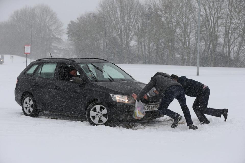 Two men help a driver try to get his car moving, after snowfalls yesterday and overnight have brought widespread disruption (PA)