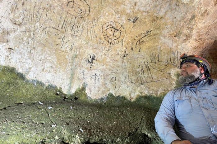 Researcher Angel Acosta-Colon, a geophysicist at the University of Puerto Rico at Arecibo, poses with a variety of pictographs, including what appears to be a lion. He believes this could be the first cave art drawn by slaves brought to Puerto Rico during Spanish colonization. Photo courtesy of Angel Acosta-Colon/The Geological Society of America