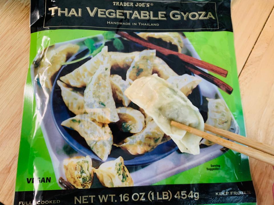 Green package of Trader Joe's frozen veggie gyoza behind chopsticks holding a dumpling