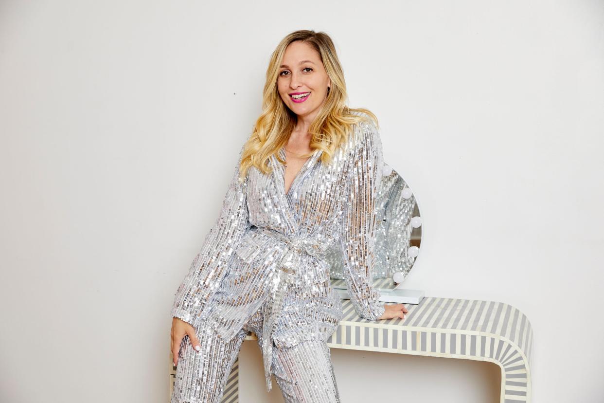 The author wearing a silver sparkly suit and leaning against a side table.