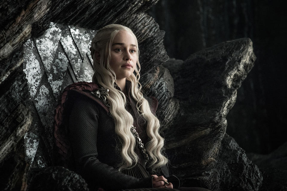 A young woman with platinum blonde hair sits on a rocky throne